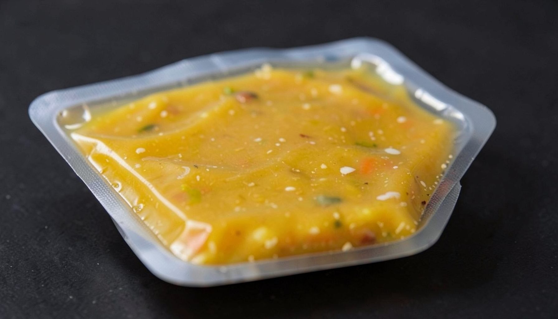 A close-up of a frozen soup base pack from Huh Pot, showing the golden broth sealed in vacuum packaging